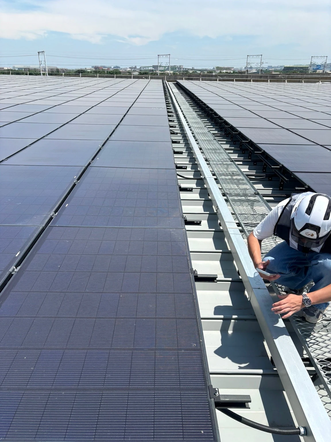 Genuine rooftop solar photograph with restrained exposure and color adjustment, showing modules and a field worker; the specific site is unconfirmed.